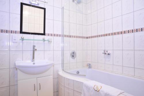a white bathroom with a sink and a bath tub at Hotel Destiny in Ongwediva