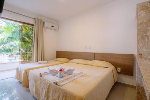 two beds in a hotel room with a window at Portal Ville - Rede Soberano in Porto Seguro