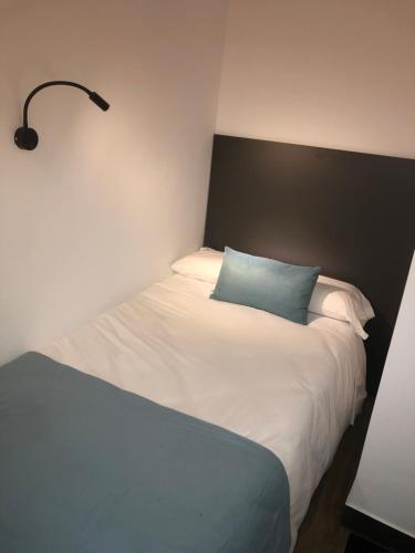 Cama blanca con almohada azul y lámpara en Loft 5 Maracena centro, en Maracena