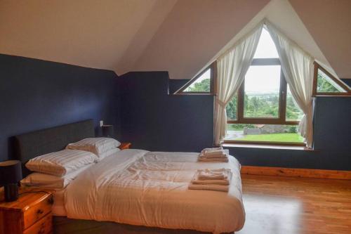 a bedroom with a large bed with two windows at The Mountain Lodge Slievenamon spacious 4 bedroom house in Cloneen