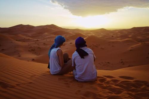 para siedząca na pustyni obserwując zachód słońca w obiekcie Erg Chigaga Camp Shooting Stars w mieście Mhamid (Amhamid al-Ghizlan)