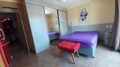 1 dormitorio con cama morada y taburete rojo en Apartamento a Duas Quadras da Praia, en Cabo Frío