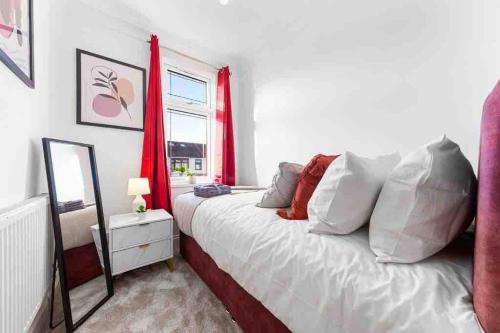 a bedroom with a bed with red curtains and a mirror at Sleeps 10, CINEMA TV , 2 baths, 10 mins to Stratford in Ilford