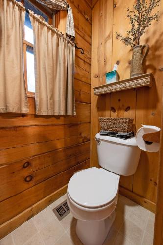 a white toilet in a wooden bathroom with a window at The Pines Riverside Log Cabin On The Ocoee in Ocoee