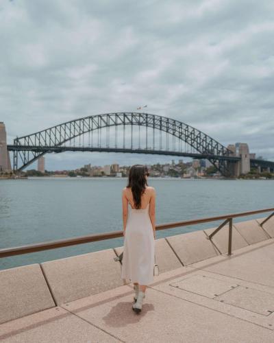 a woman in a white dress walking in front of a bridge at Paradox Sydney in Sydney
