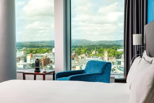 a bedroom with a bed and a blue chair and a window at Radisson Blu Hotel, Cardiff in Cardiff