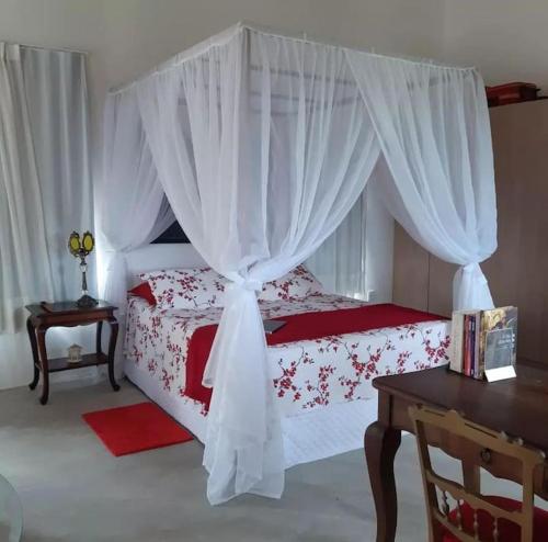 um quarto com uma cama com cortinas brancas e uma mesa em Chalé romântico, com vista panorâmica, para Casais em Monte das Gameleiras