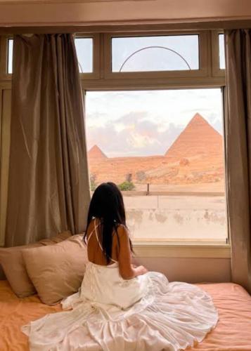 Sphinx view hotel في Ghaţāţī: فتاة صغيرة جالسة على سرير وتطل على نافذة
