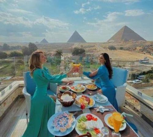 two women sitting at a table with food in front of pyramids at Sphinx view hotel in Ghaţāţī