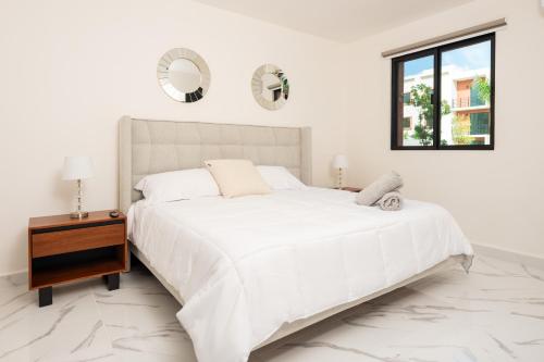 Un dormitorio blanco con una cama grande y una mesa en 2BR Moderno en residencial Ombu en Cancún