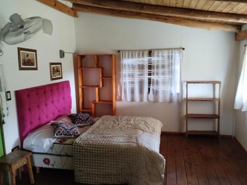 1 dormitorio con 1 cama con cabecero rosa y ventana en Las Chunas en Villa Yacanto