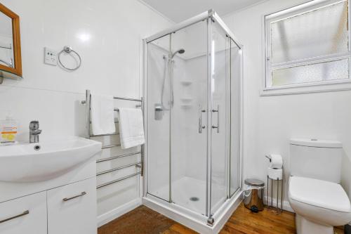 a white bathroom with a shower and a sink at Back of Beyond Cottage in Rotoiti