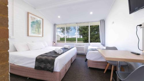 a bedroom with two beds and a table and a desk at Tahmoor Inn in Tahmoor