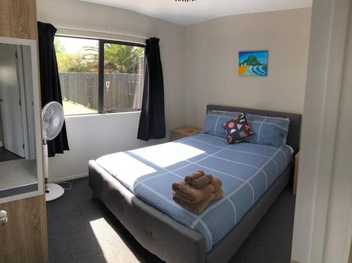 a bedroom with a bed with blue sheets and a window at Whitianga Kiwi Bach in Whitianga