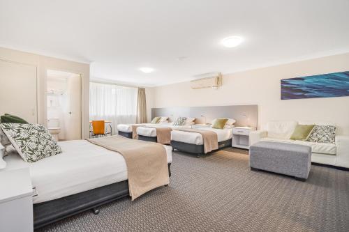 una habitación de hotel con tres camas y un sofá en Cosmo Motel Adamstown, en Newcastle