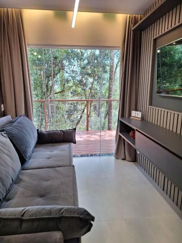 a living room with a couch and a large window at Chalé Sabiá - Refúgio Cantos da Serra in Campos do Jordão