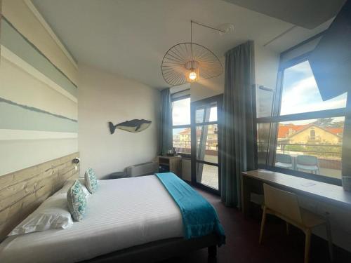 a bedroom with a bed and a desk and a window at Baya Hotel in Capbreton