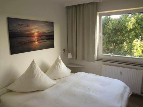 ein weißes Bett mit Kissen in einem Schlafzimmer mit Fenster in der Unterkunft Rimmler - Südstrandperle in Westerland