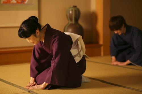 a woman kneeling on the floor in front of a priest at Kotonoyado Musashino in Nara