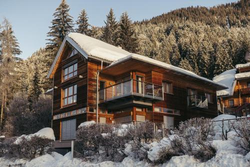 a large wooden house in the snow with trees at Appartementhotel am Weissensee in Weissensee