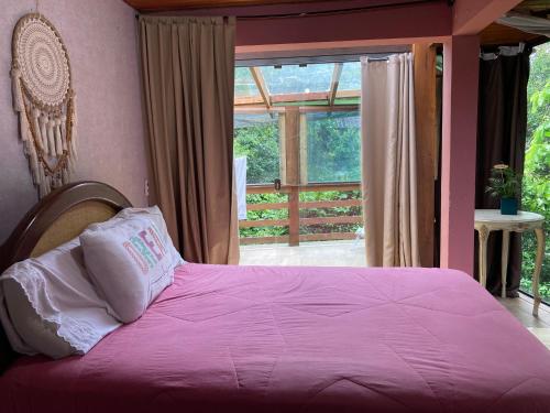 sypialnia z łóżkiem z różową pościelą i oknem w obiekcie Shanti Yoga Forest House w mieście Florianópolis