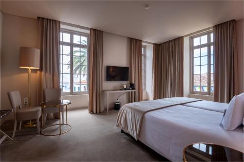um quarto de hotel com uma cama, uma secretária e janelas em Vila Gale Collection S.Miguel em Ponta Delgada
