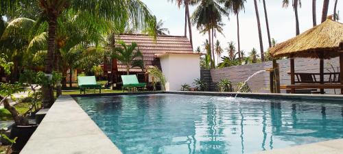 a swimming pool with chairs and a house with palm trees at Pandan Bungalow in Gili Air