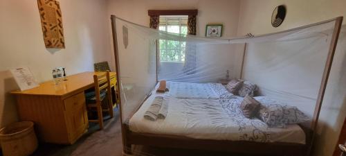 1 dormitorio con cama con dosel y escritorio en Mutolere Coffee Pot Guest Houses en Kisoro