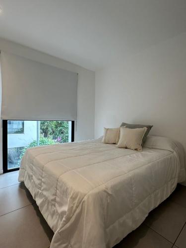 a white bedroom with a large bed with a window at Departamento Güemes in Mar del Plata