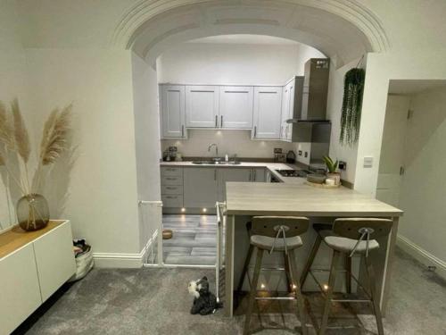 a kitchen with white cabinets and a kitchen island with two bar stools at Orange Rentals- Cosy Apartment- Free Parking! in Liverpool