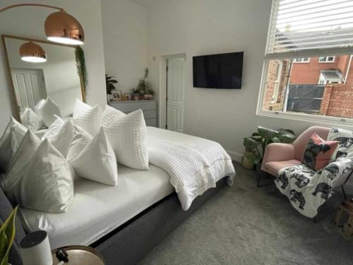 a bedroom with a bed with white pillows and a chair at Orange Rentals- Cosy Apartment- Free Parking! in Liverpool