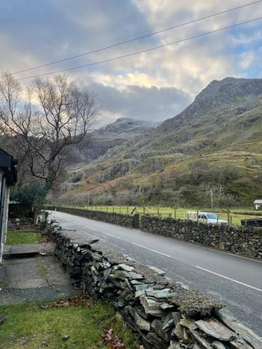 a road with a stone wall next to a mountain at Terfyn Cottage in Dinorwic