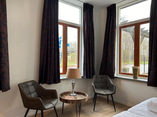 Hotel Nijeveen في Nijeveen: غرفة نوم بها كرسيين وطاولة ونوافذ