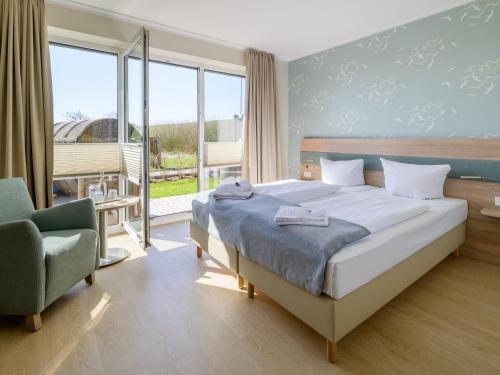 a bedroom with a bed and a chair and windows at Nordsee-Hotel Arlau-Schleuse in Husum