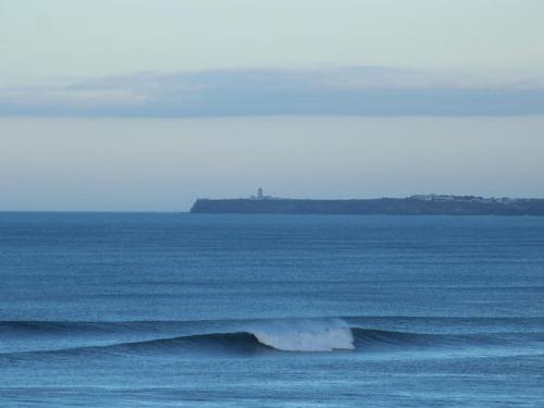 a wave in the ocean with an island in the distance at Tiny House Eloá in Lourinhã