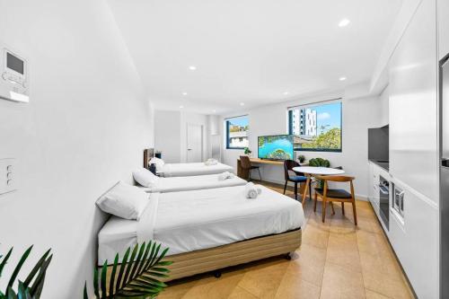 a white bedroom with two beds and a table at Lovely Studio apartments in Strathfield CBD in Sydney
