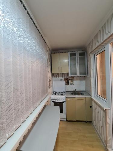 una pequeña cocina con electrodomésticos blancos y una ventana en уютная квартира, en Shymkent