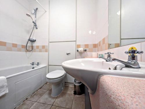 a bathroom with a sink and a toilet and a tub at Hitchin Priory Hotel in Hitchin