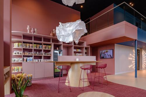 a library with pink walls and stools and a bar at ibis Styles Rotterdam Ahoy in Rotterdam