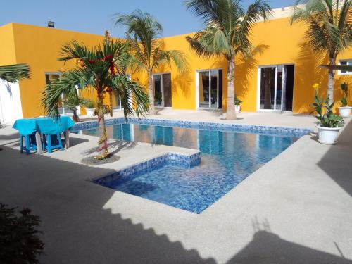 a swimming pool with palm trees and a yellow building at Hôtel Colibri in Niaga