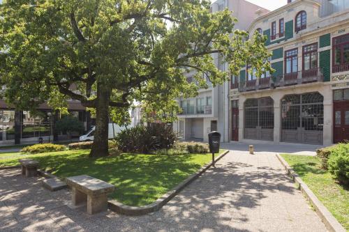 a park with benches and a tree in front of a building at QP Trindade Apartments in Porto
