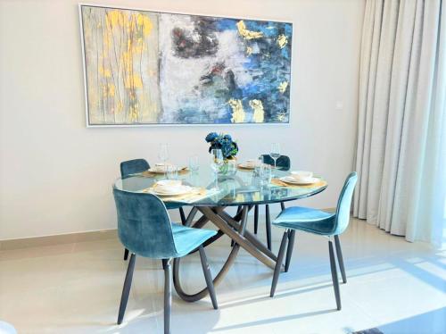 a dining room with a glass table and blue chairs at Luxurious Creek Harbour Apt with Balcony & View in Dubai