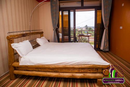 um quarto com uma cama de madeira com lençóis brancos e uma varanda em Amicus Hotel Kampala em Kireka