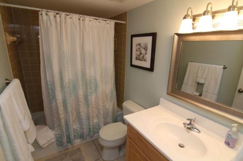 een badkamer met een wastafel, een toilet en een spiegel bij Visit this top floor property located on the no-drive beach with 2 complex pools! in New Smyrna Beach