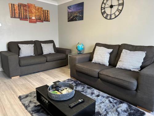 una sala de estar con 2 sofás y un reloj en la pared en Modern Cosy Warm Home With Free Parking, en Chelmsford