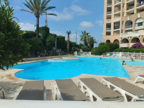 une grande piscine avec des chaises longues et un bâtiment dans l'établissement Ciel Bleu de Cannes - Appartement Vue Azur avec Piscines et Jardin, à Cannes