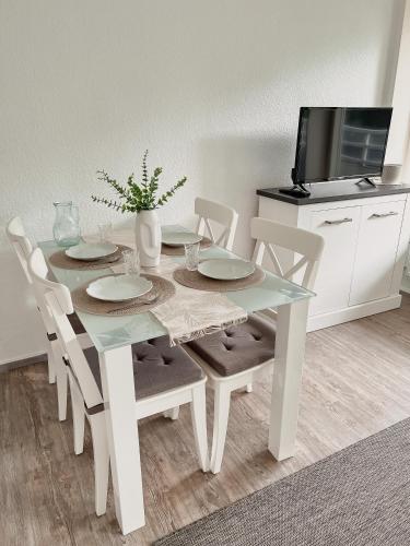 mesa de comedor blanca con sillas y TV en Strandnahe Wohnung mit Meerblick, en Sierksdorf