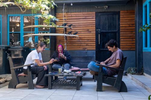 three people sitting on a bench in front of a building at LÖF Hostal in Pichilemu