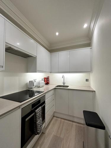a kitchen with white cabinets and a sink at Chic Studio Flat 8 Mins to Harrods Knightsbridge in London