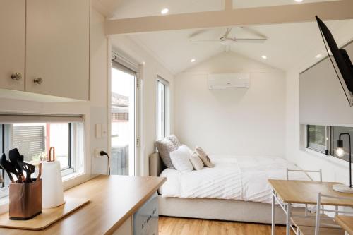 a white bedroom with a bed and a table at Sweet beautiful TINY HOME with pool and 2 minute drive to the beach in Wollongong